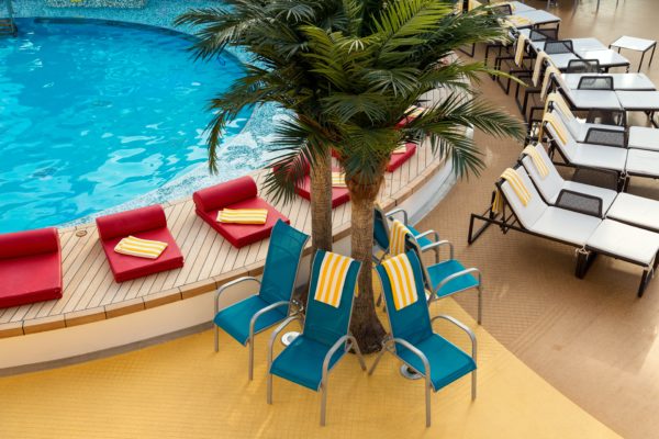 pool deck on a cruise ship with colorful lounge chairs and palm trees