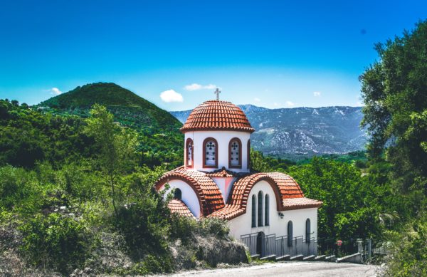 A church in Greece surrounded by green mountains and a deep blue sky