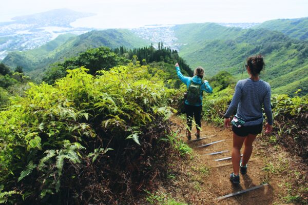 two women hiking down a mountain surrounded by green plants