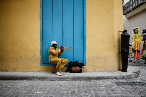 man in Cuba playing trumpet on street corner next to vibrant colored building