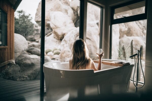 woman relaxing in a spa tub holding a glass of wine, enjoying the view of a rocky, outdoor landscape