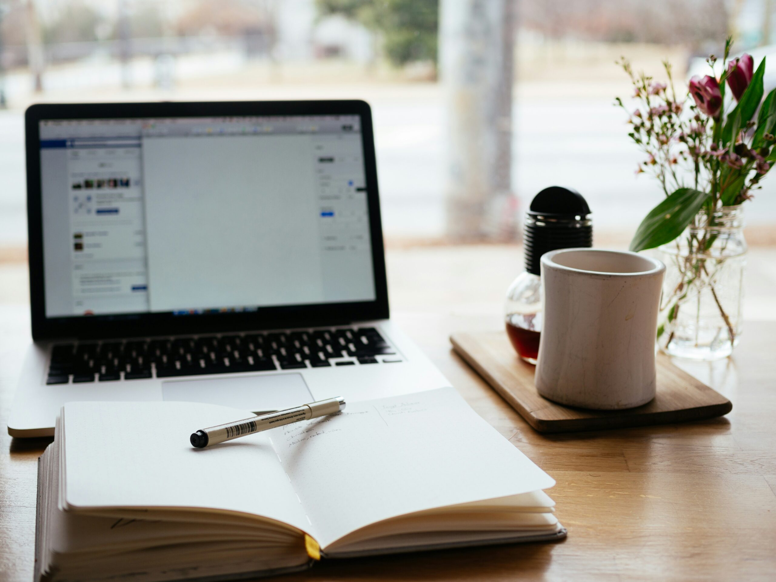 laptop open with a notebook in front and a mug of coffee on the side