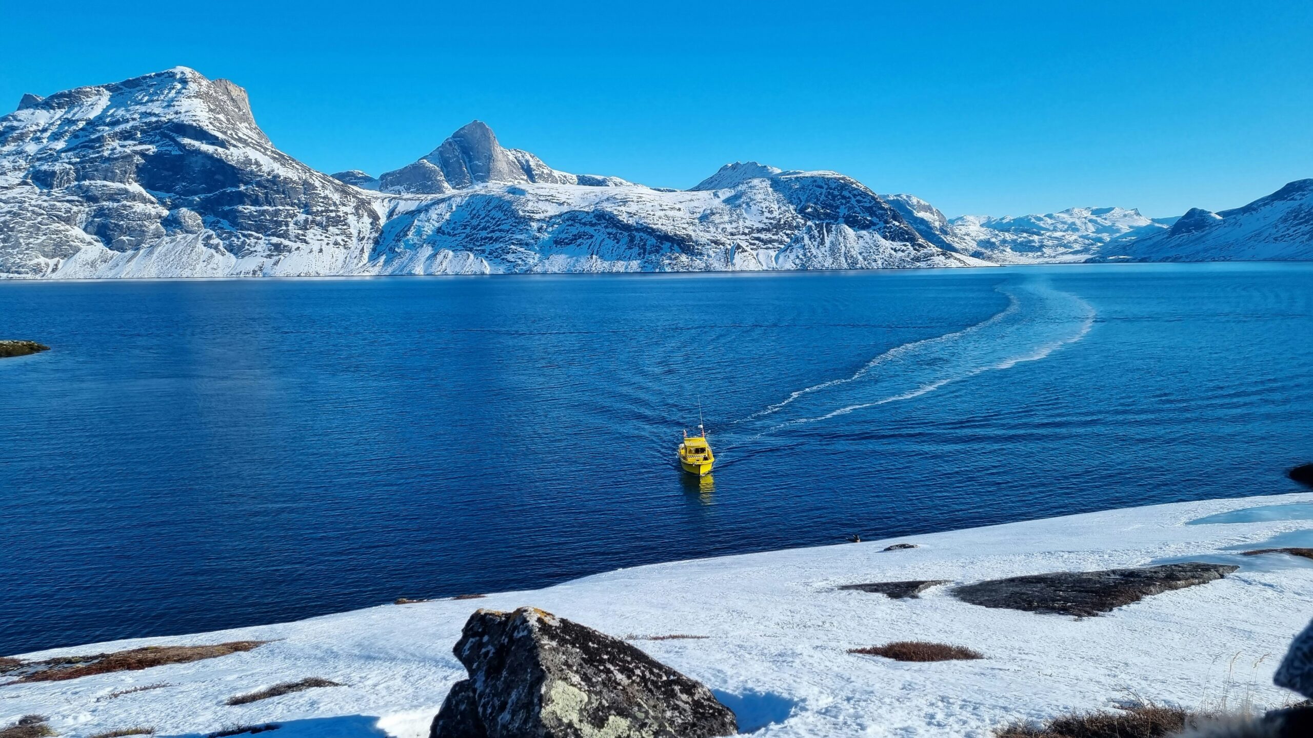 blue waters in Greenland with snowcapped bluffs in the background
