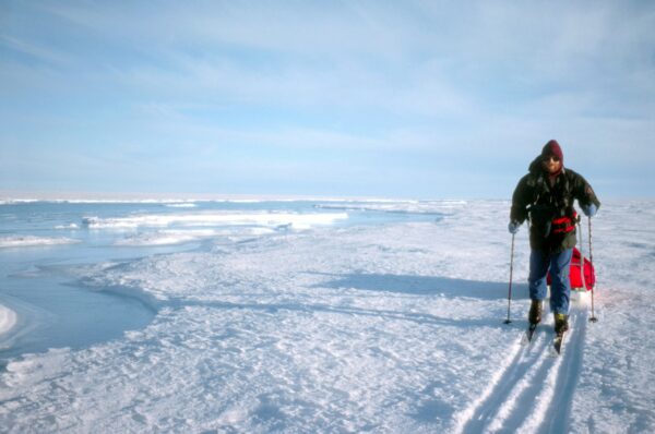 man in Greenland on an actic excursion in the snow with skis and ski poles pulling a sled