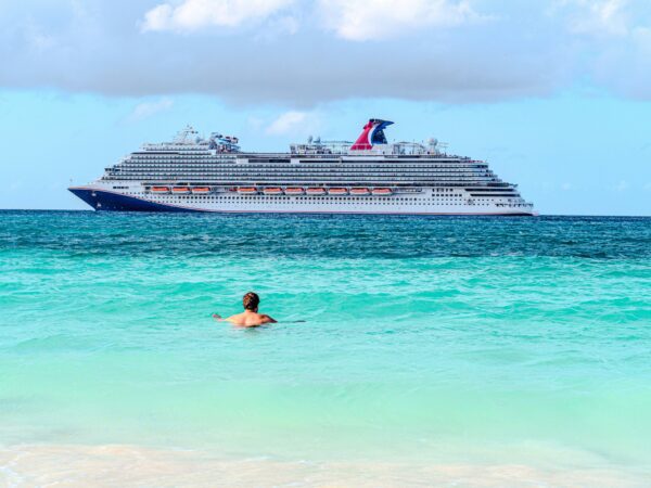 man swimming in turquoise blue water with a large cruise ship off in the distance in front of the man