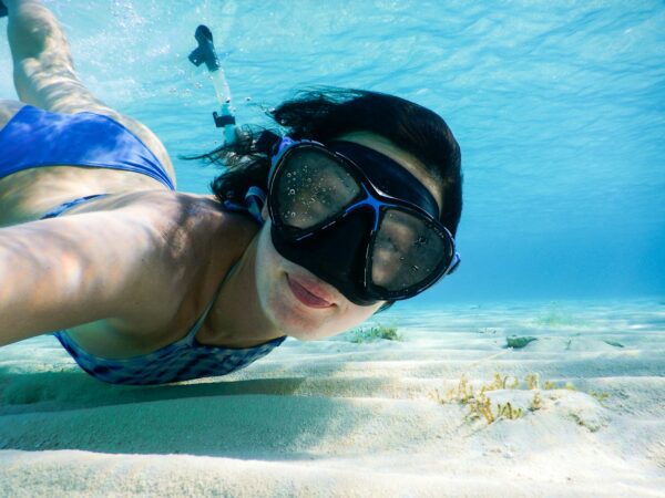 girl snorkeling at bottom of ocean with snorkeling mask and swimsuite