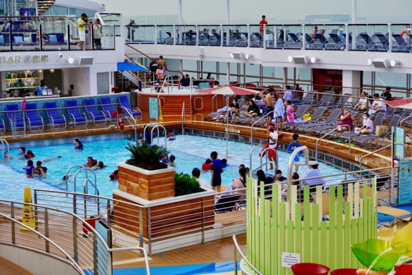 pool deck on a cruise ship with people in chairs and also people swimming in the pool