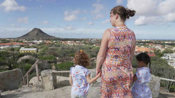 a mom holding hands with her two small daughters overlooking landscape with a mountain or volcano in the distance