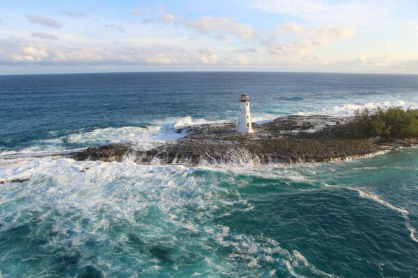 lighthouse next to sea with water foaming next to the land