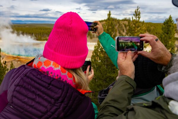 three people wearing winter gear taking pictures with their phones of a northern landscape