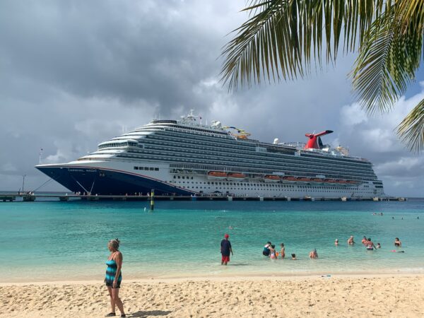 cruise ship docked at a port with some people swimming in the nearby ocean and the sky looks like it may storm