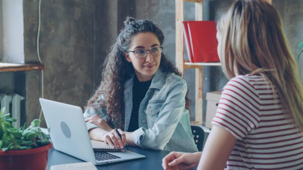 two women at desk one with laptop and the other facing away