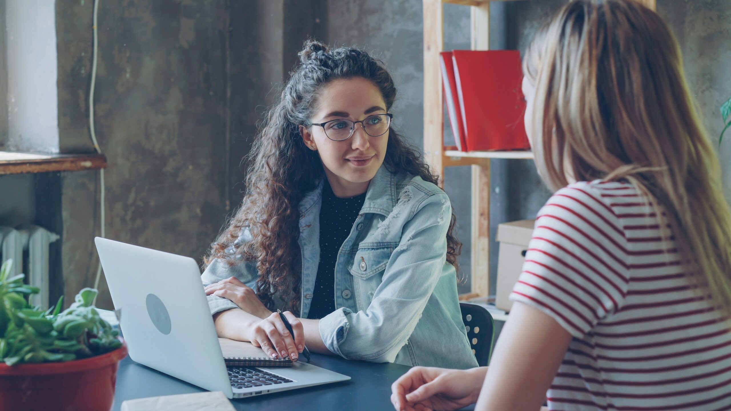 two women facing each other and one is using a laptop