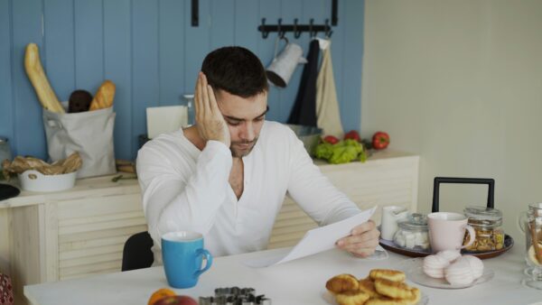 man at breakfast table surrounded by breakfast foods looking down at a paper he's holding looking worried