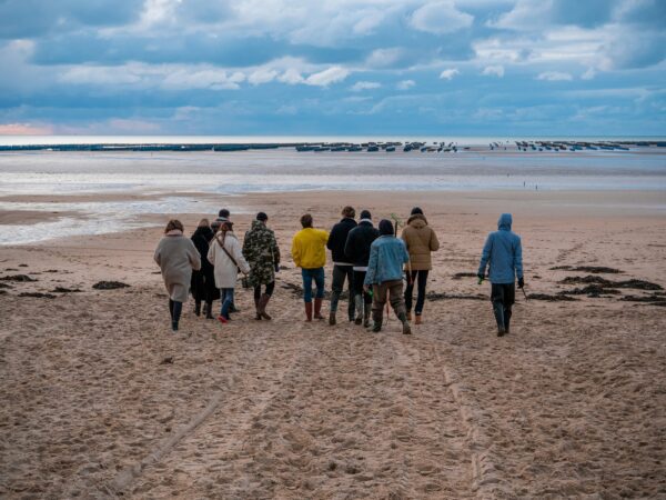 group of travelers on a sandy area all wearing jackets looking out at the scenery