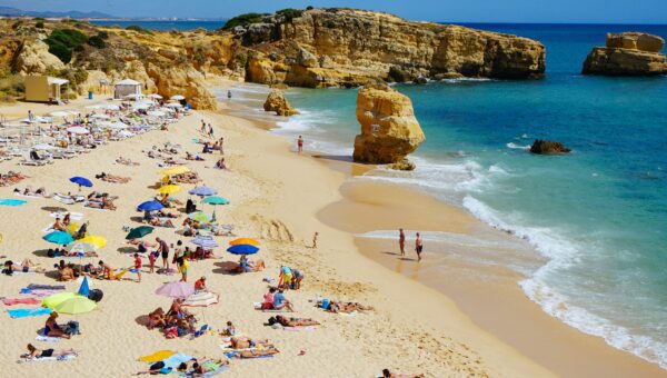 beach with turquoise blue water and people with umbrellas on sand in Portugal