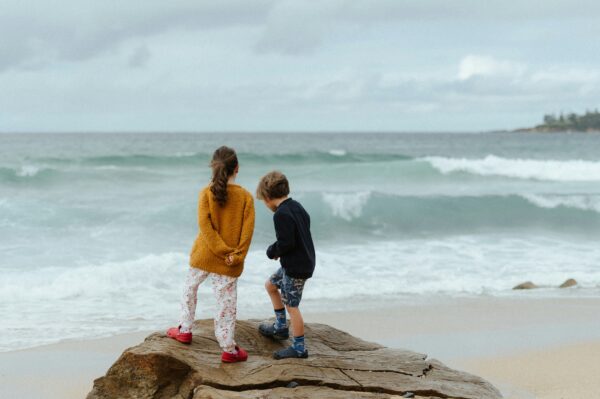 two school-age children standing on a large rock overlooking the ocean