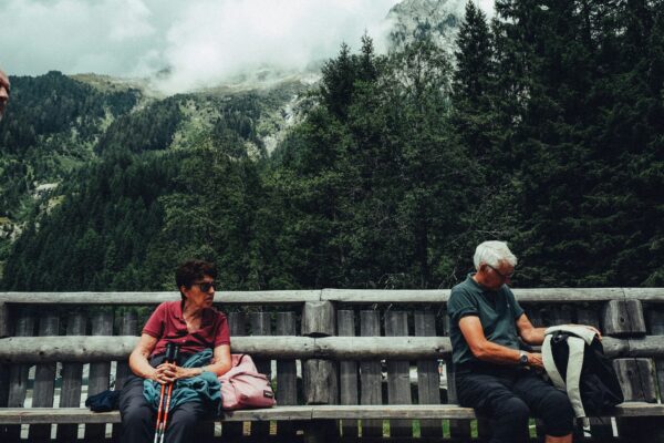an older couple sitting on a wooden log bench in the mountains with hiking gear