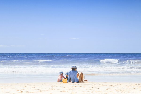 a family sitting on the beach with two small children playing in the sand